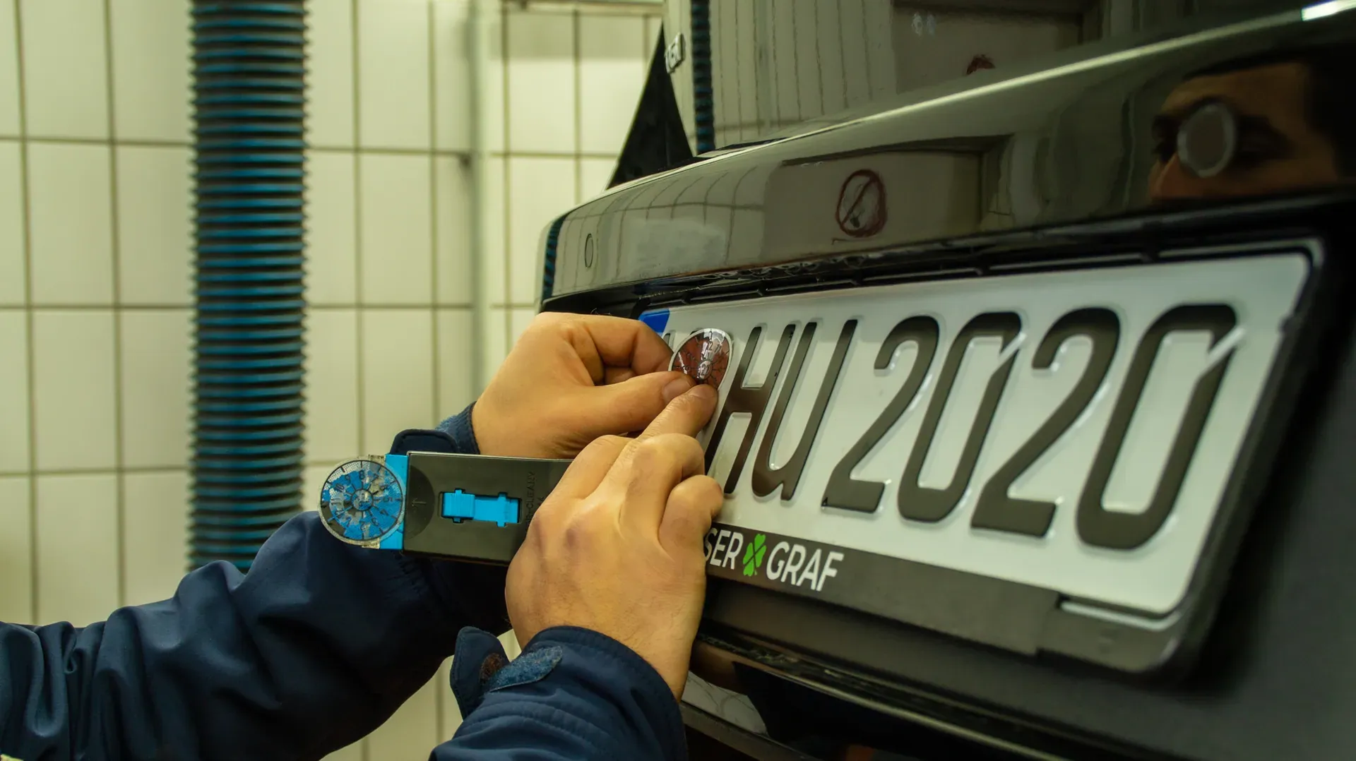 Prüfingenieur klebt die neue HU-Plakette auf, Prüfhalle der Kfz-Prüfstelle HU Plus in Nürnberg